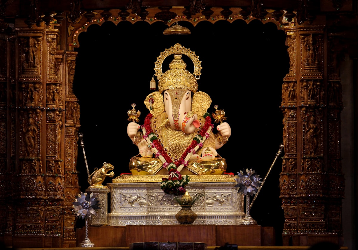 Golden Ganesha idol with flower garland in ornate wooden shrine — Ganesh Chaturthi 2026 temple